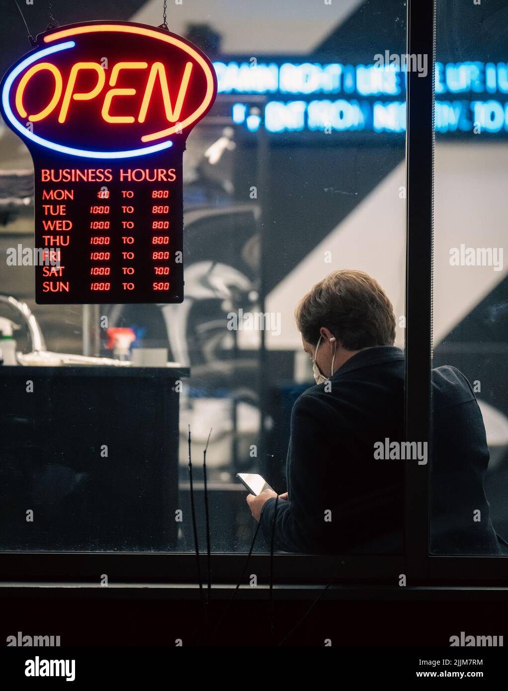 Un maschio seduto accanto a un segno 'aperto' nel barbiere e controllare il suo telefono cellulare in Canada Foto Stock