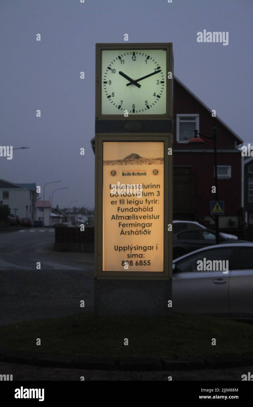 Una bella foto di una pubblicità sotto un orologio pubblico a Keflavik, Islanda contro un cielo grigio tramonto Foto Stock