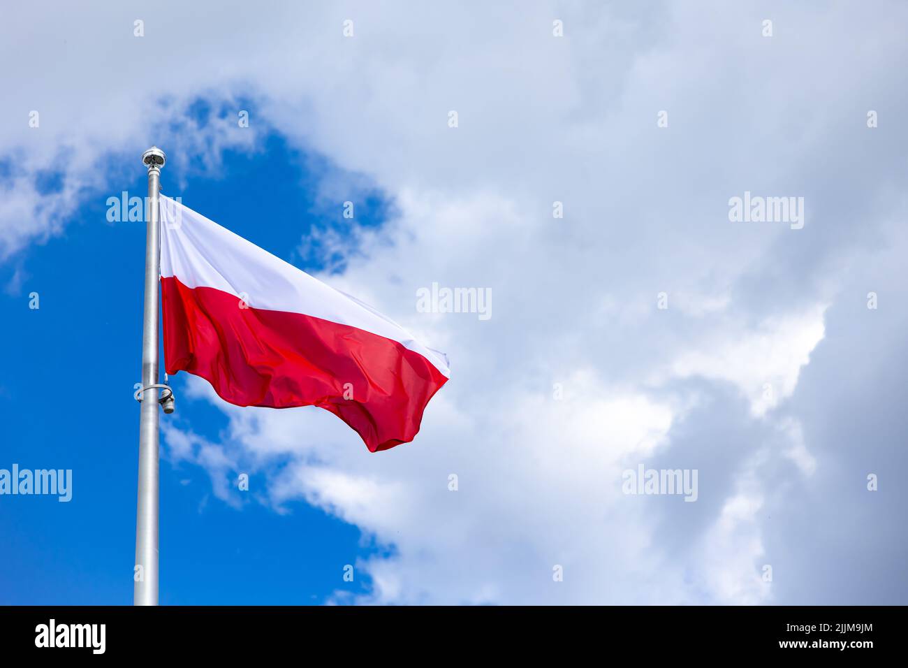 Bandiera nazionale della Polonia ondita sullo sfondo del cielo blu con piccole nuvole. Foto scattata a metà giornata. Foto Stock