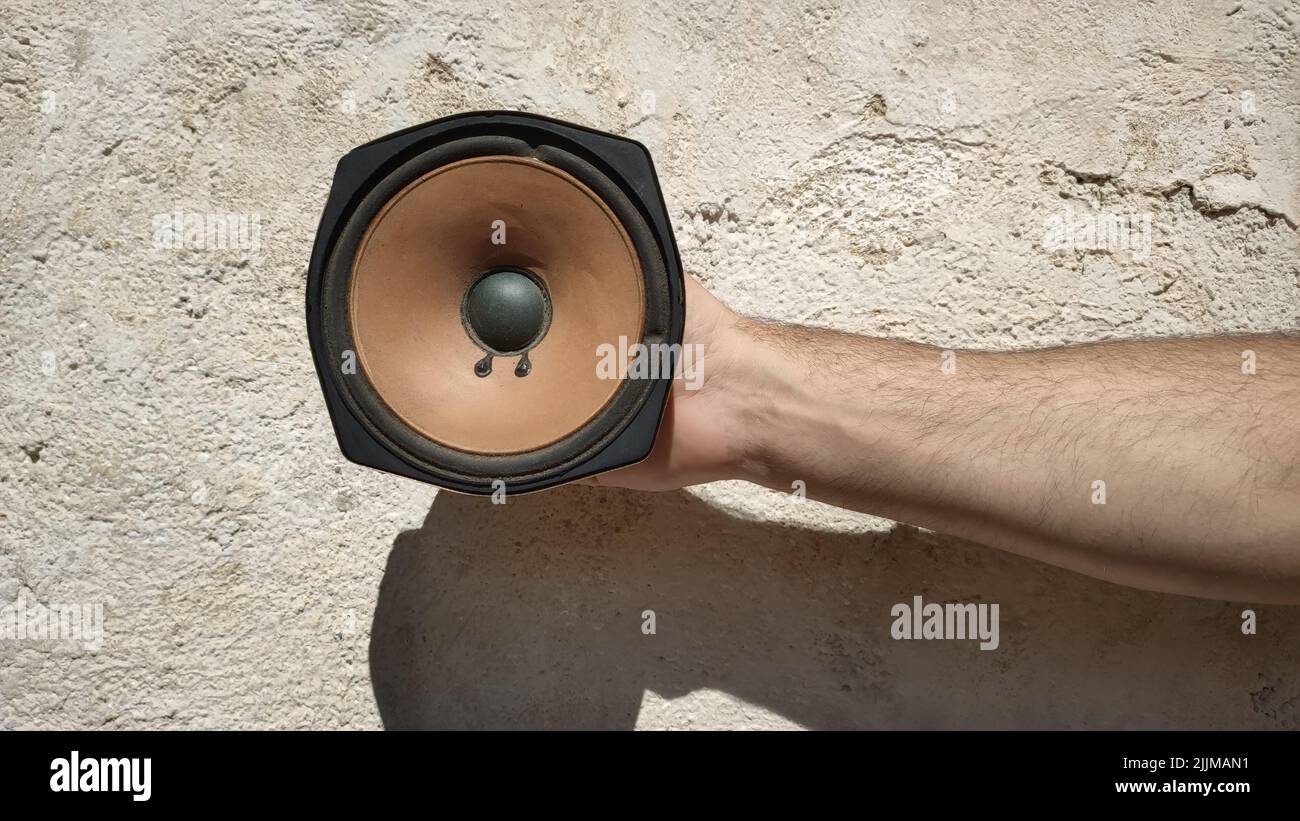 Una mano di un uomo che tiene un vecchio altoparlante davanti ad un muro Foto Stock Una mano di un uomo che tiene un vecchio altoparlante davanti ad un muro Foto Stock