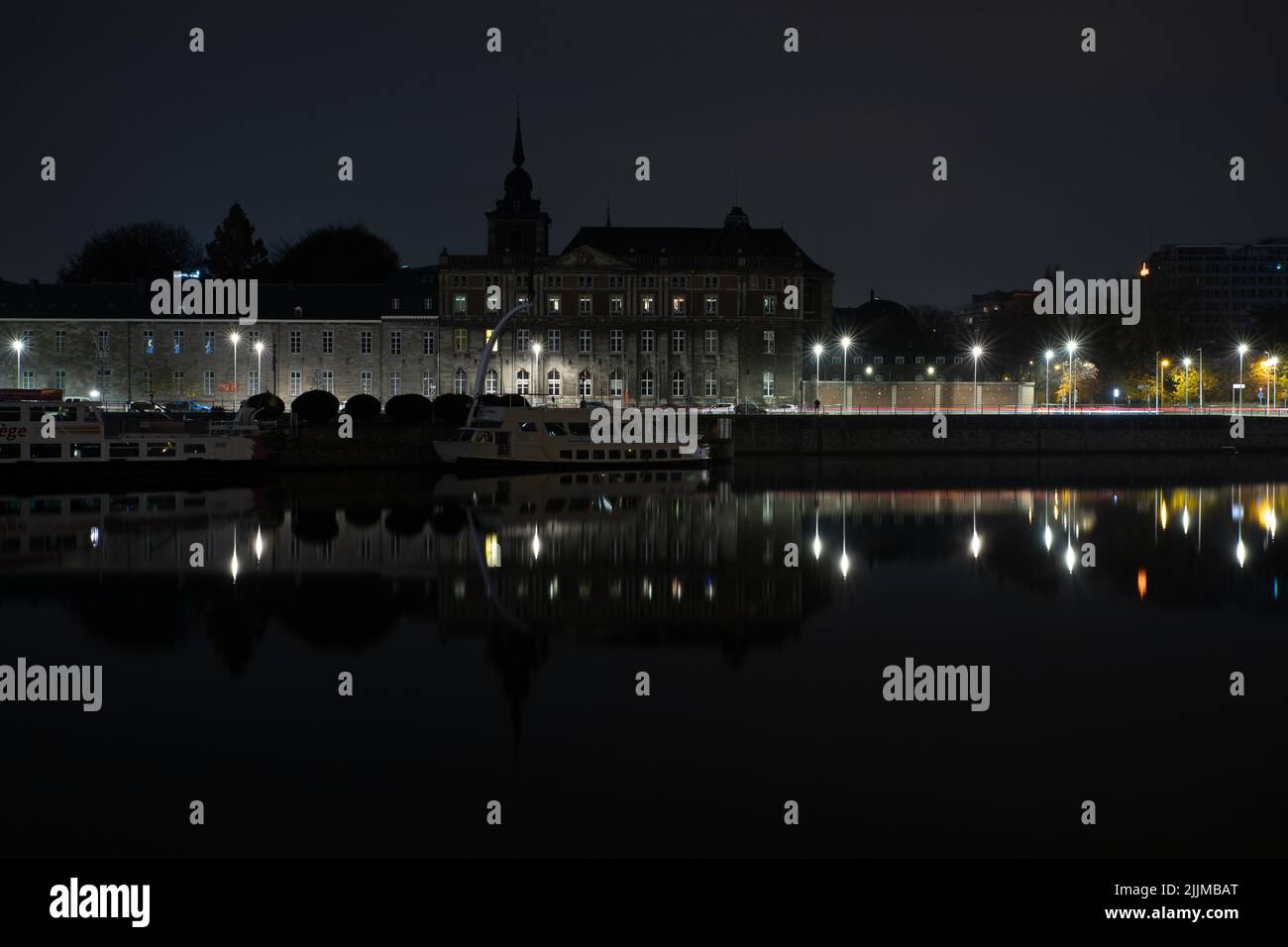 Un edificio storico e le navi si riflettono nell'acqua di notte a Liegi, in Belgio Foto Stock