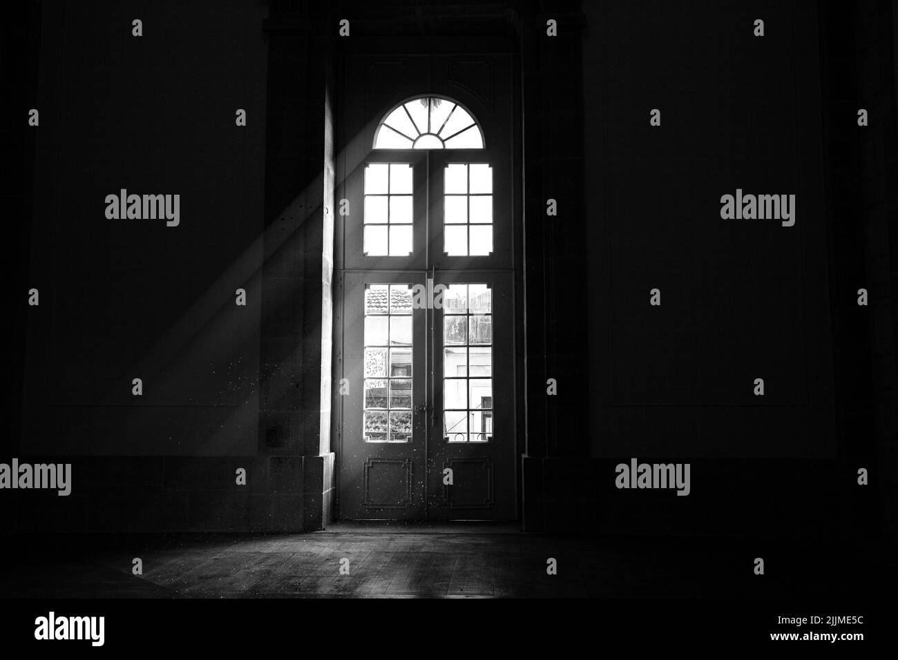 Un'immagine in scala di grigi della luce che entra attraverso una porta Foto Stock