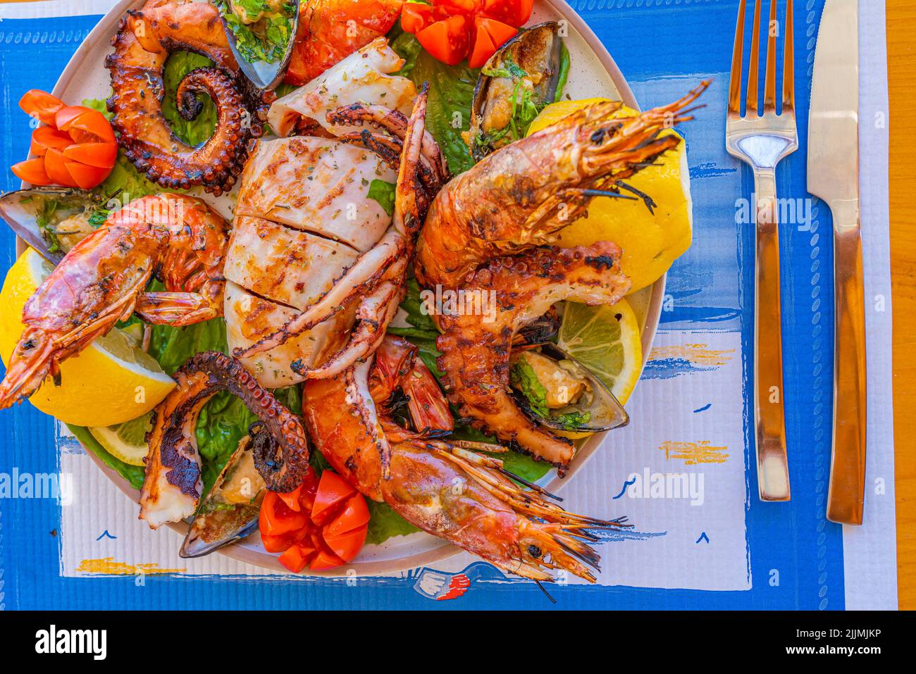 Piatto di pesce con calamari alla griglia, polpo, gamberi e cozze su insalata verde con limone e pomodoro Foto Stock