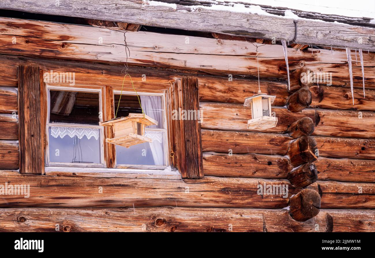 Un bel colpo di una vecchia casa di legno con gli alimentatori di uccelli e la caduta di neve e una piccola finestra Foto Stock