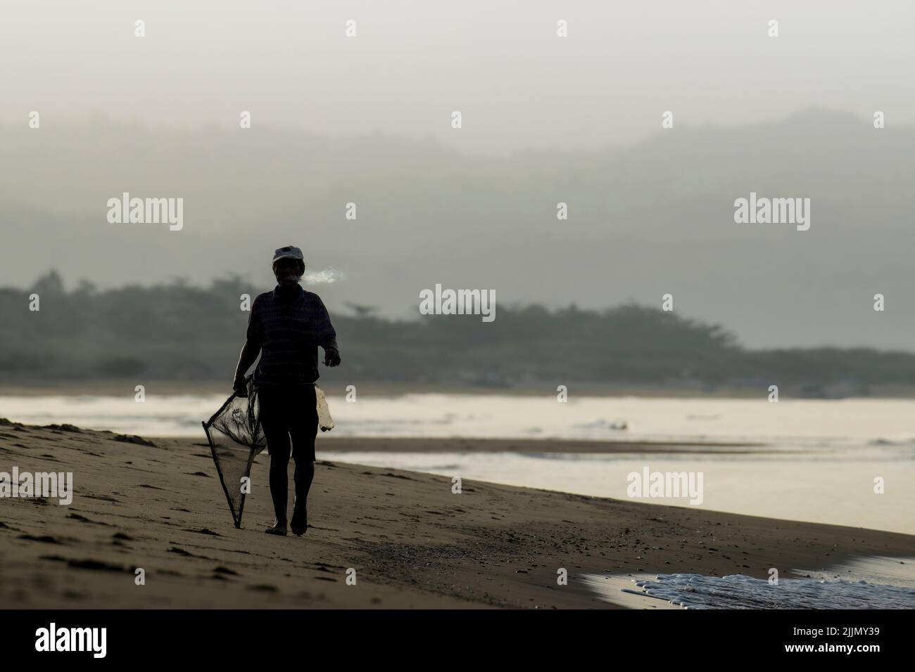 Un uomo con sagome cammina sulla riva mattina per prepararsi alla sua routine di pesca in una giornata di nebbia Foto Stock