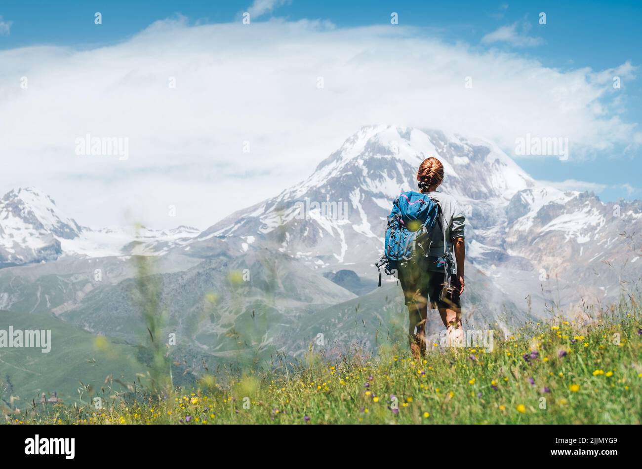 Donna Backpacker con uno zaino in piedi e godere di piste innevate di montagna Kazbek 5054m mentre lei cammina da verde erba collina. Moun del Caucaso orientale Foto Stock