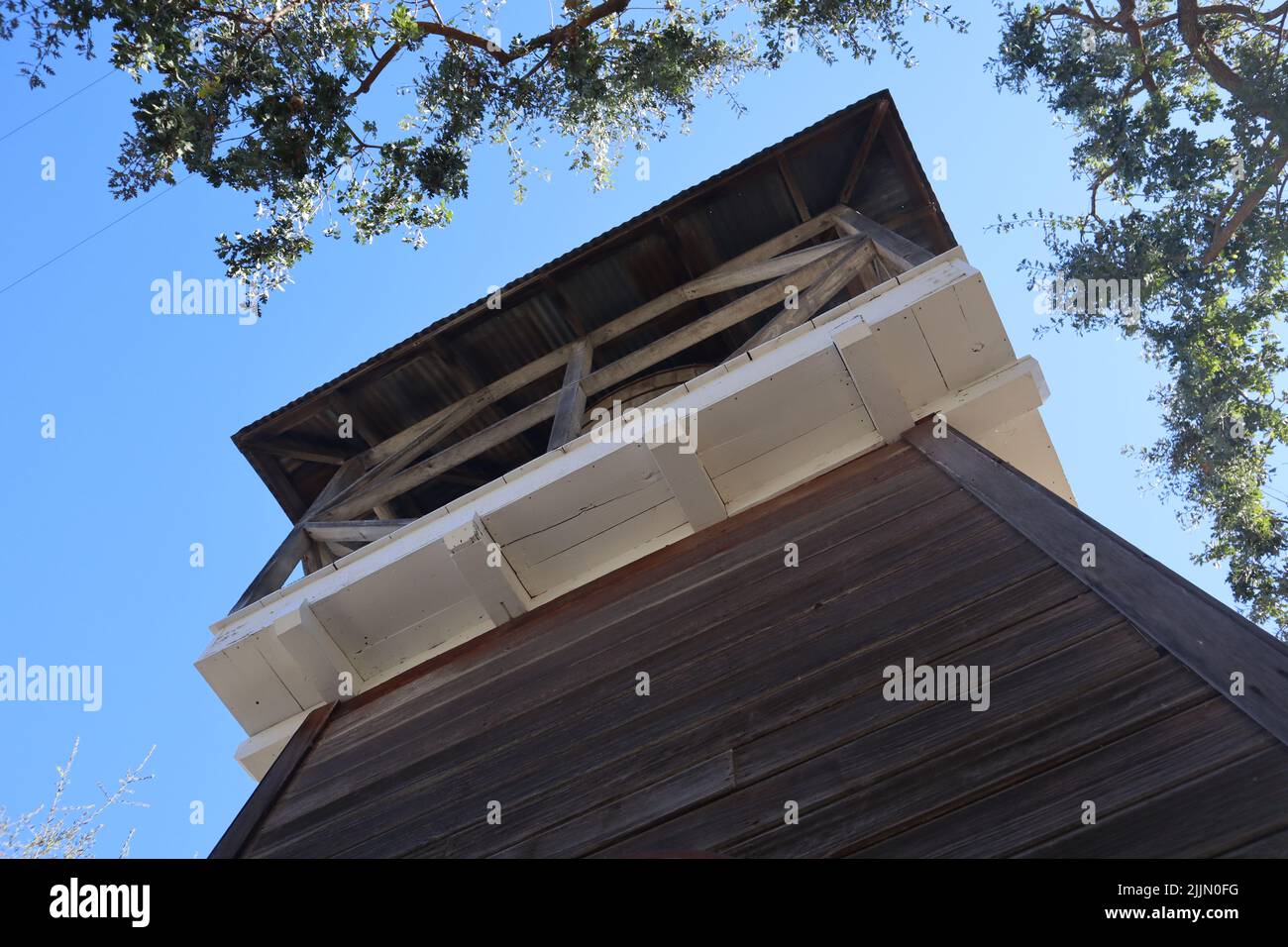Un piccolo angolo di una torre d'acqua in legno tra gli alberi contro il cielo blu senza nuvole Foto Stock