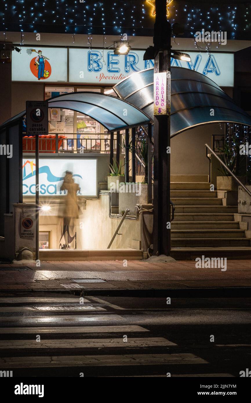 Un colpo verticale di una persona sfocata che cammina in un negozio di notte. Foto Stock