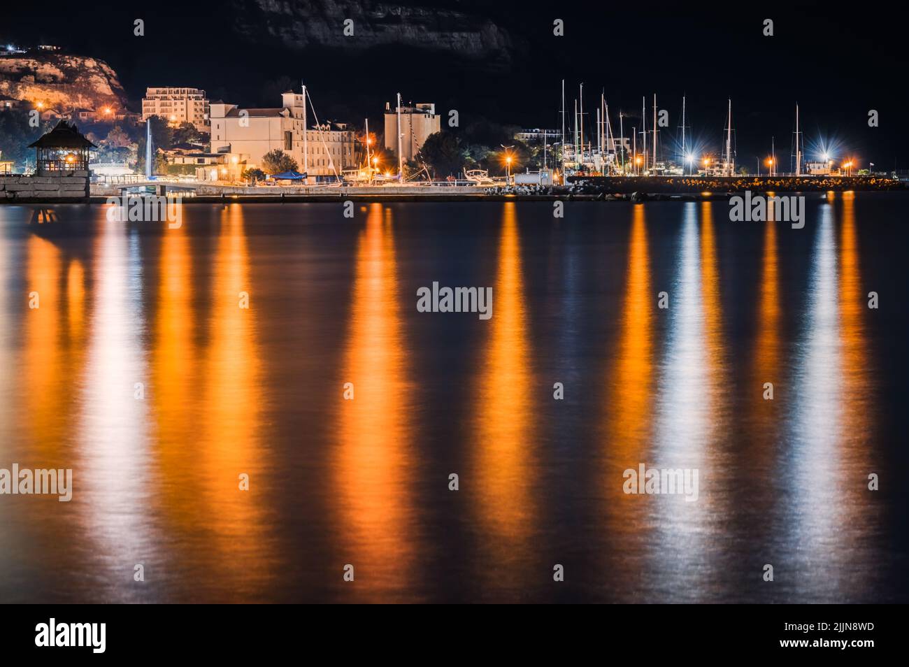 Una vista panoramica degli edifici vicino a un porto con le luci riflesse sull'acqua in Balchik, Bulgaria Foto Stock