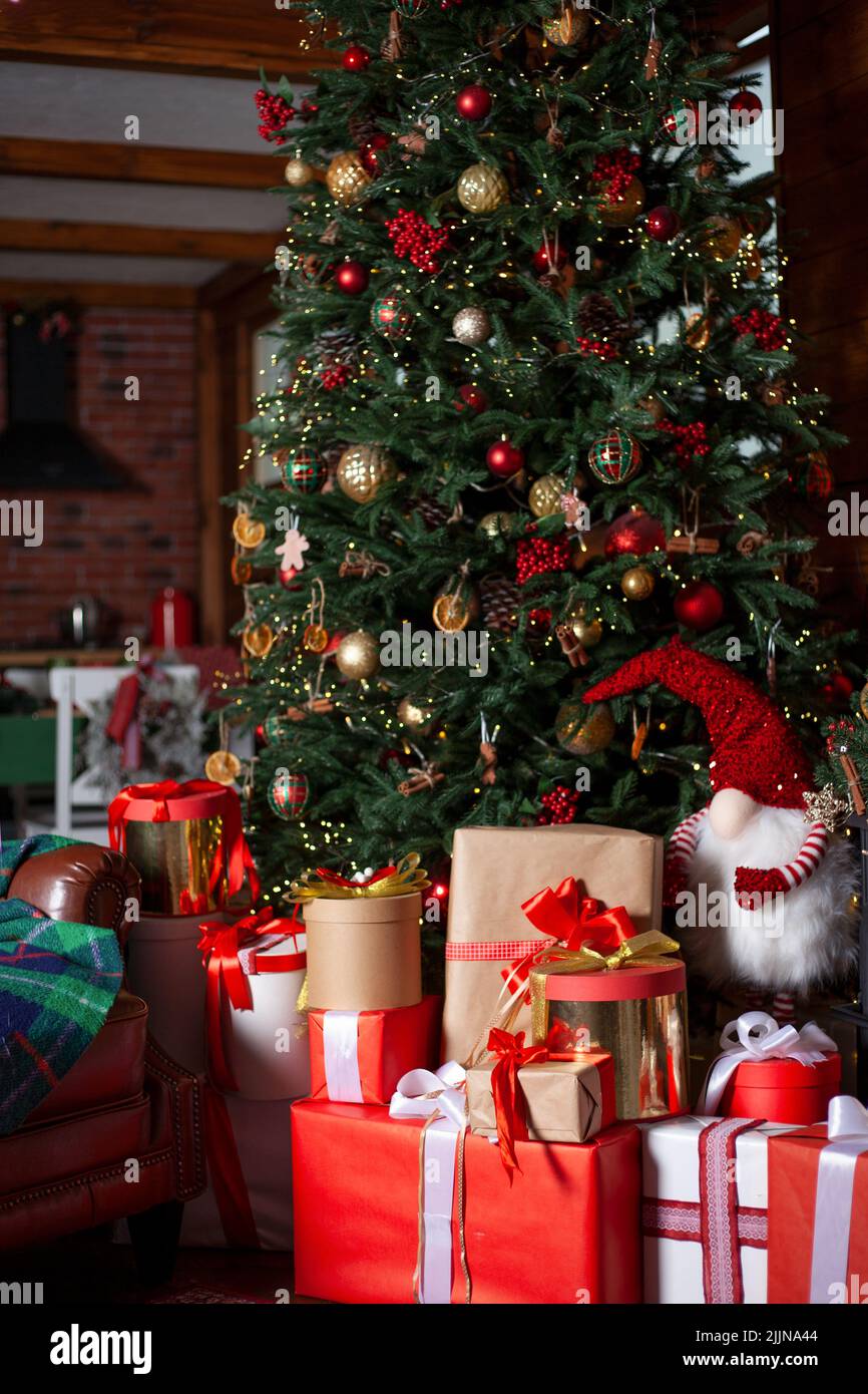 Albero di Natale con luci e regali. Regalo in confezione rossa. Casa accogliente vacanza. L'atmosfera del nuovo anno. Sfondo di Natale. Foto Stock