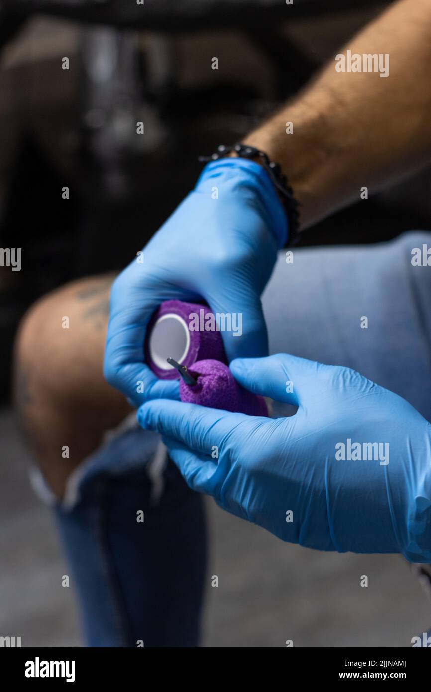 Un primo piano di mani maschili di un tatuatore che prepara una macchina da tatuaggio prima di fare un tatuaggio Foto Stock