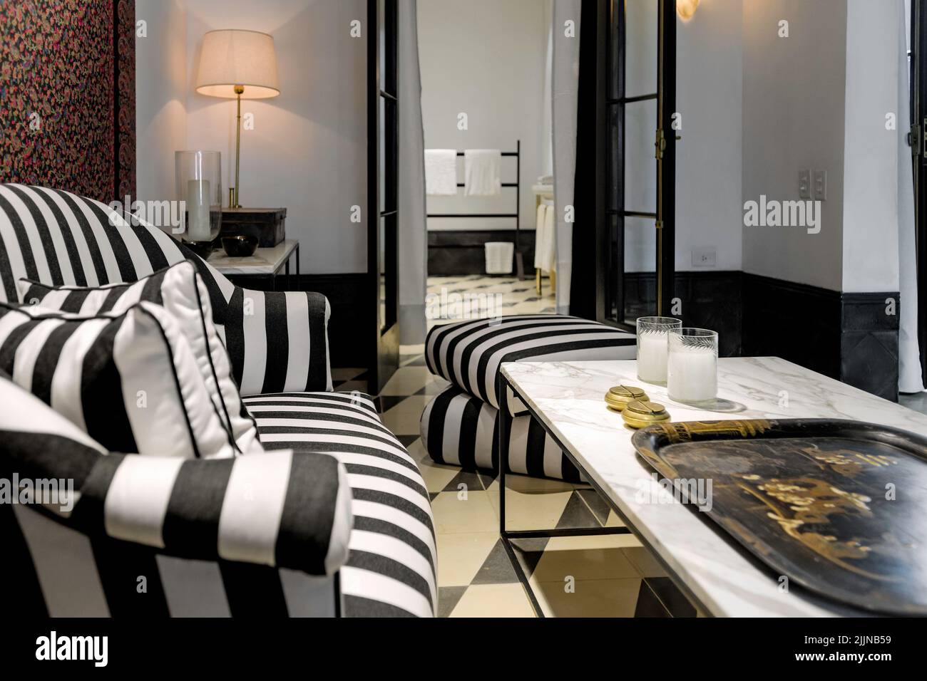 Un piccolo soggiorno in stile eclettico con un divano a righe, tavolo in marmo e asciugamani da bagno sullo sfondo. Foto Stock