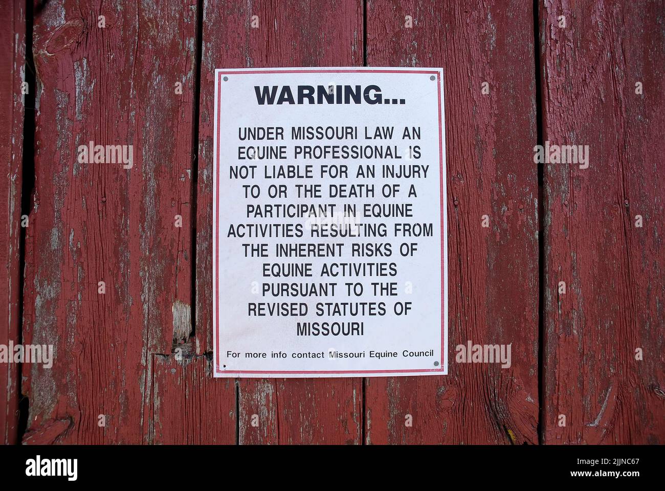 Un cartello segnaletico che fa riferimento alle responsabilità legali di un impianto equino su una porta di legno rosso grunge Foto Stock