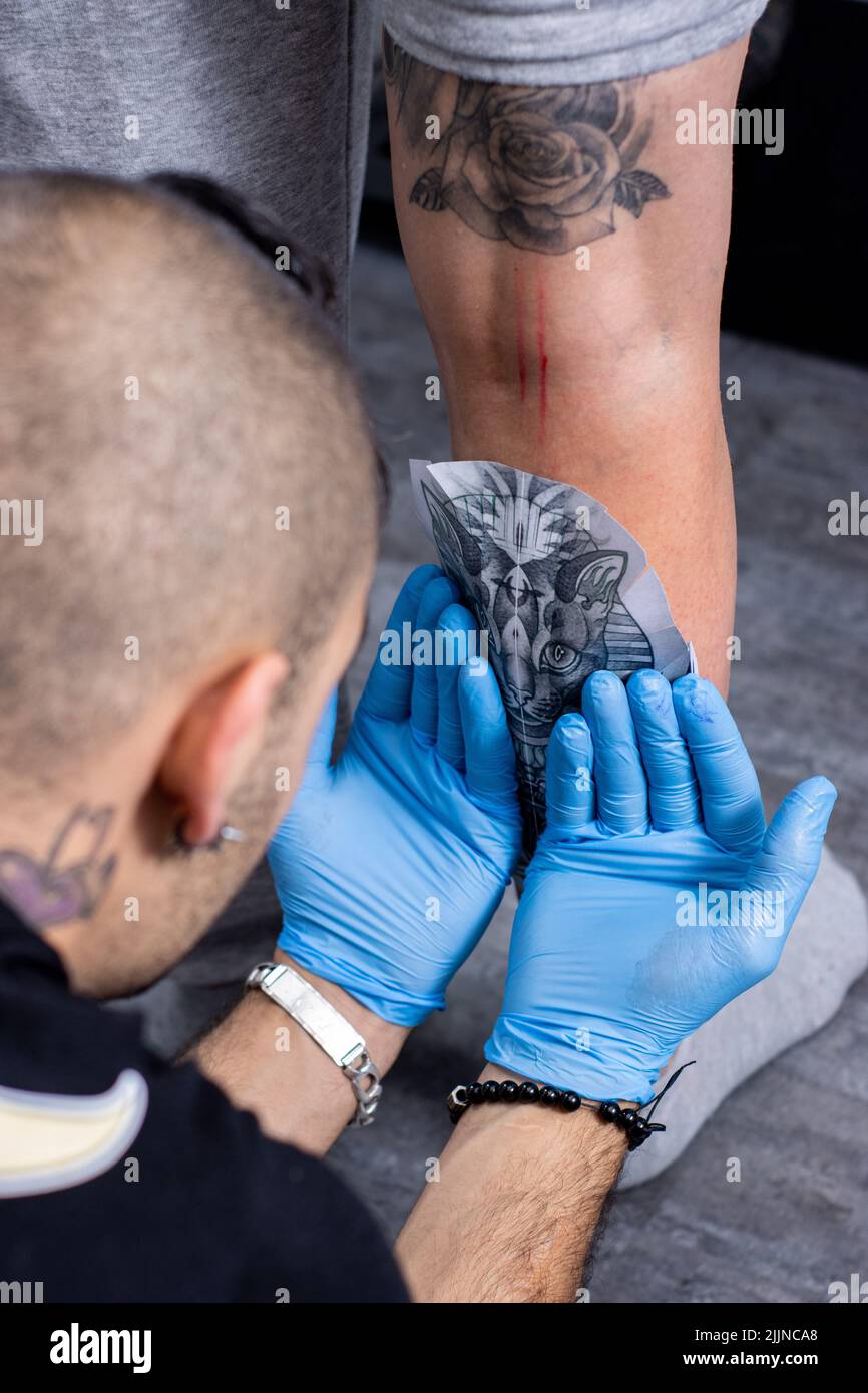 Un tatuatore che mette la carta da ricalco dalla gamba di un cliente pronto per il tatuaggio in uno studio di tatuaggio Foto Stock