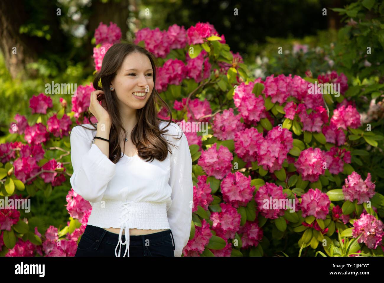 Un primo piano di una donna caucasica vicino al cespuglio di fiori di rosa Foto Stock