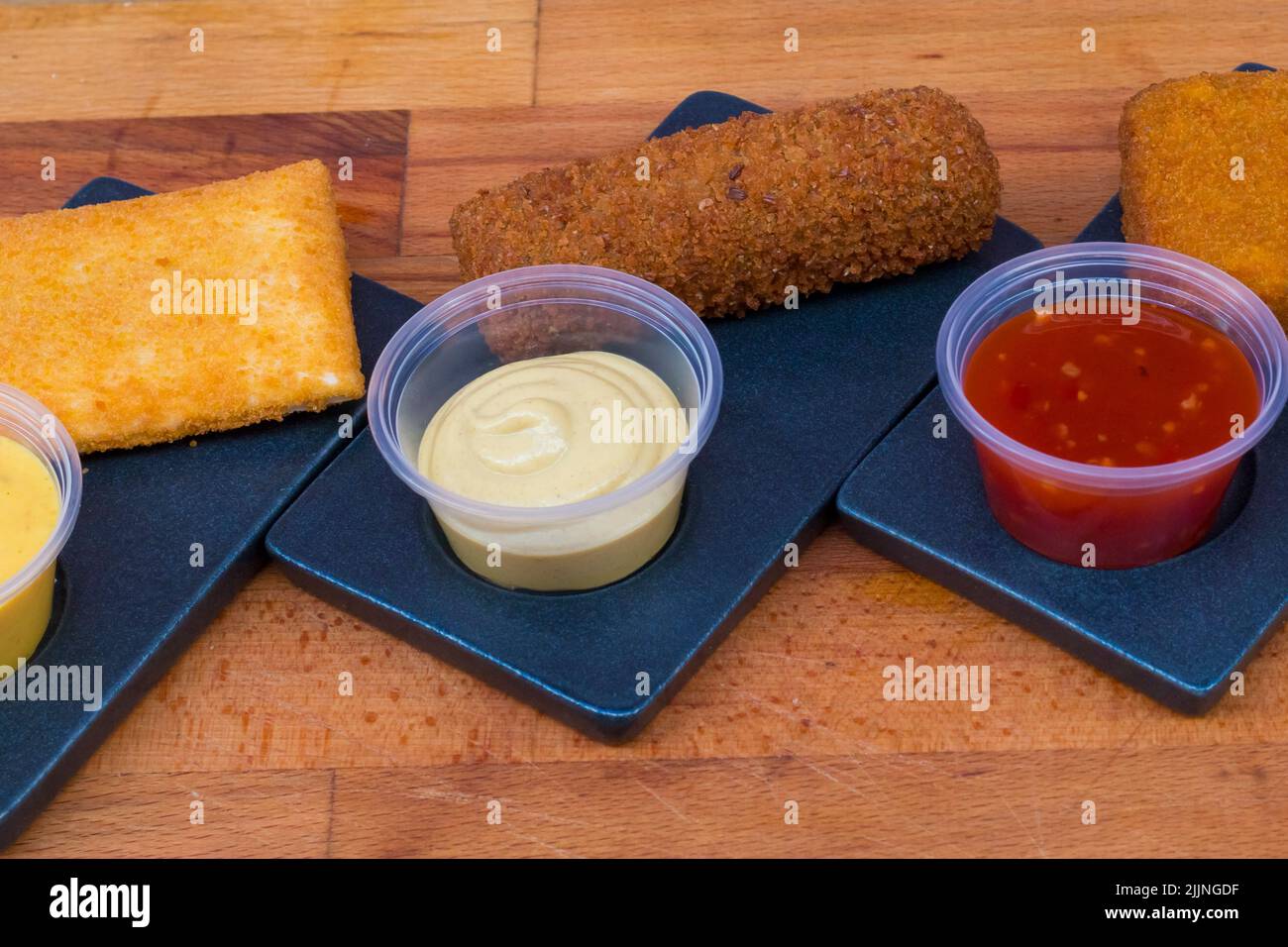 I diversi tipi di pepite croccanti fritte con salse su un piatto nero Foto Stock