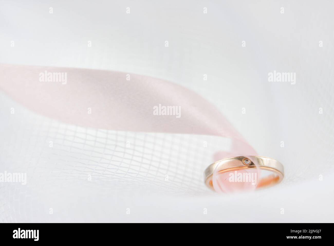 Un primo piano di un anello di nozze con un nastro rosa su sfondo bianco Foto Stock