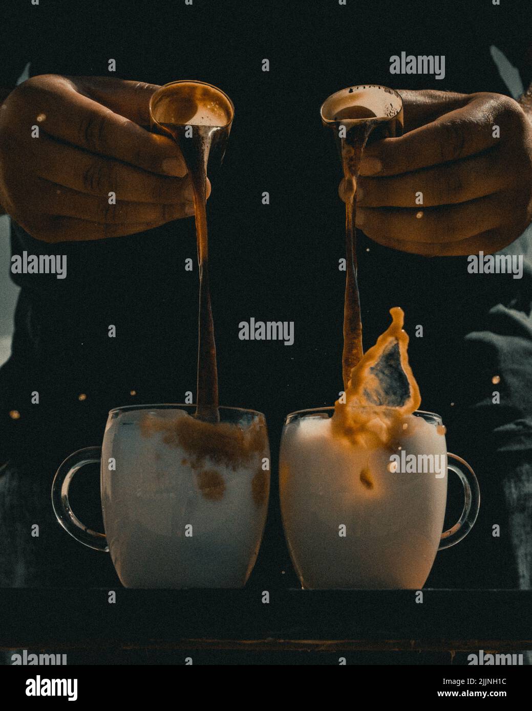 Una verticale di un barista che versa il caffè nelle tazze di vetro riempite di latte Foto Stock