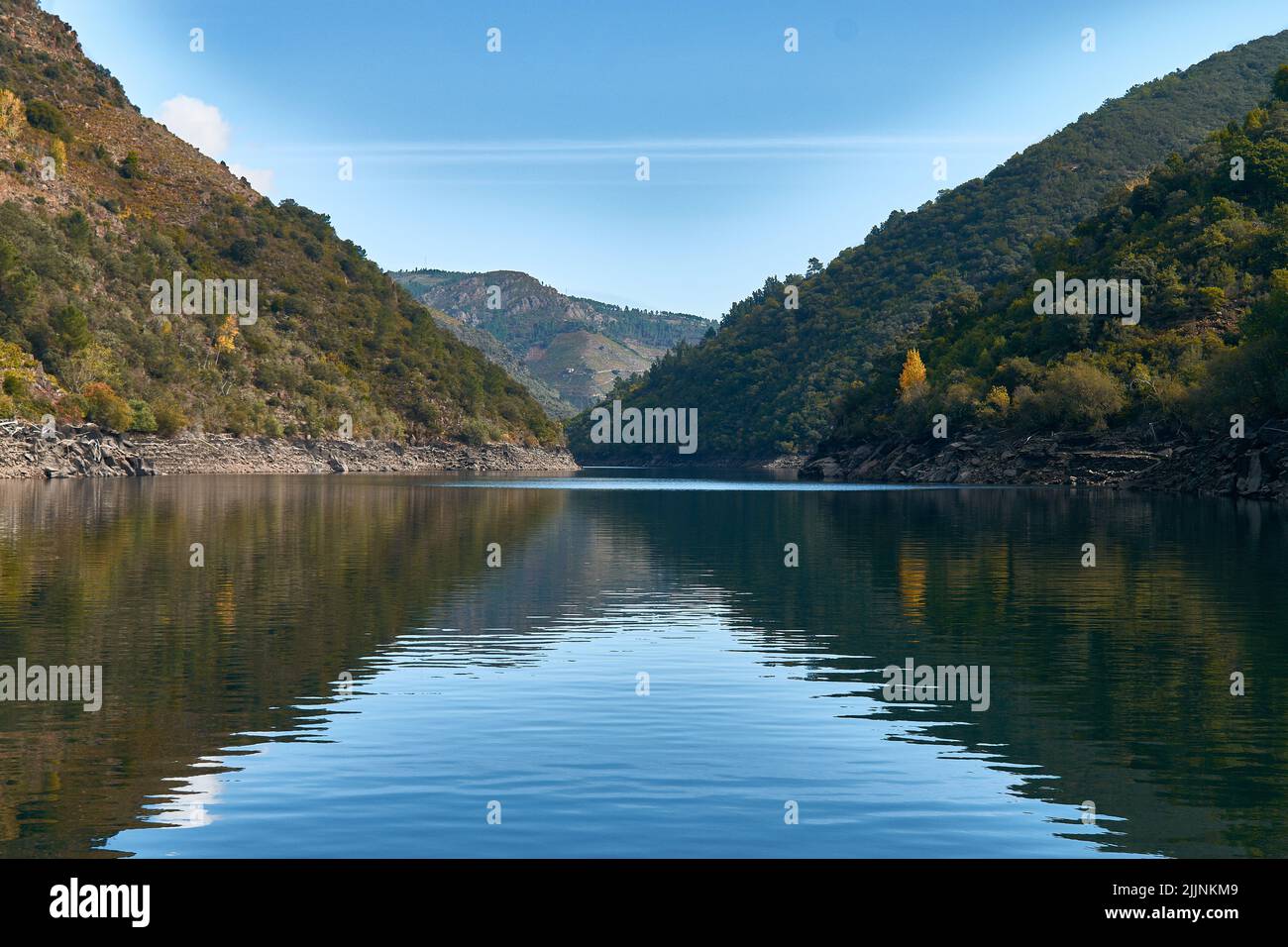 Un paesaggio mozzafiato di un lago tranquillo tra montagne forestali durante una mattinata di sole Foto Stock