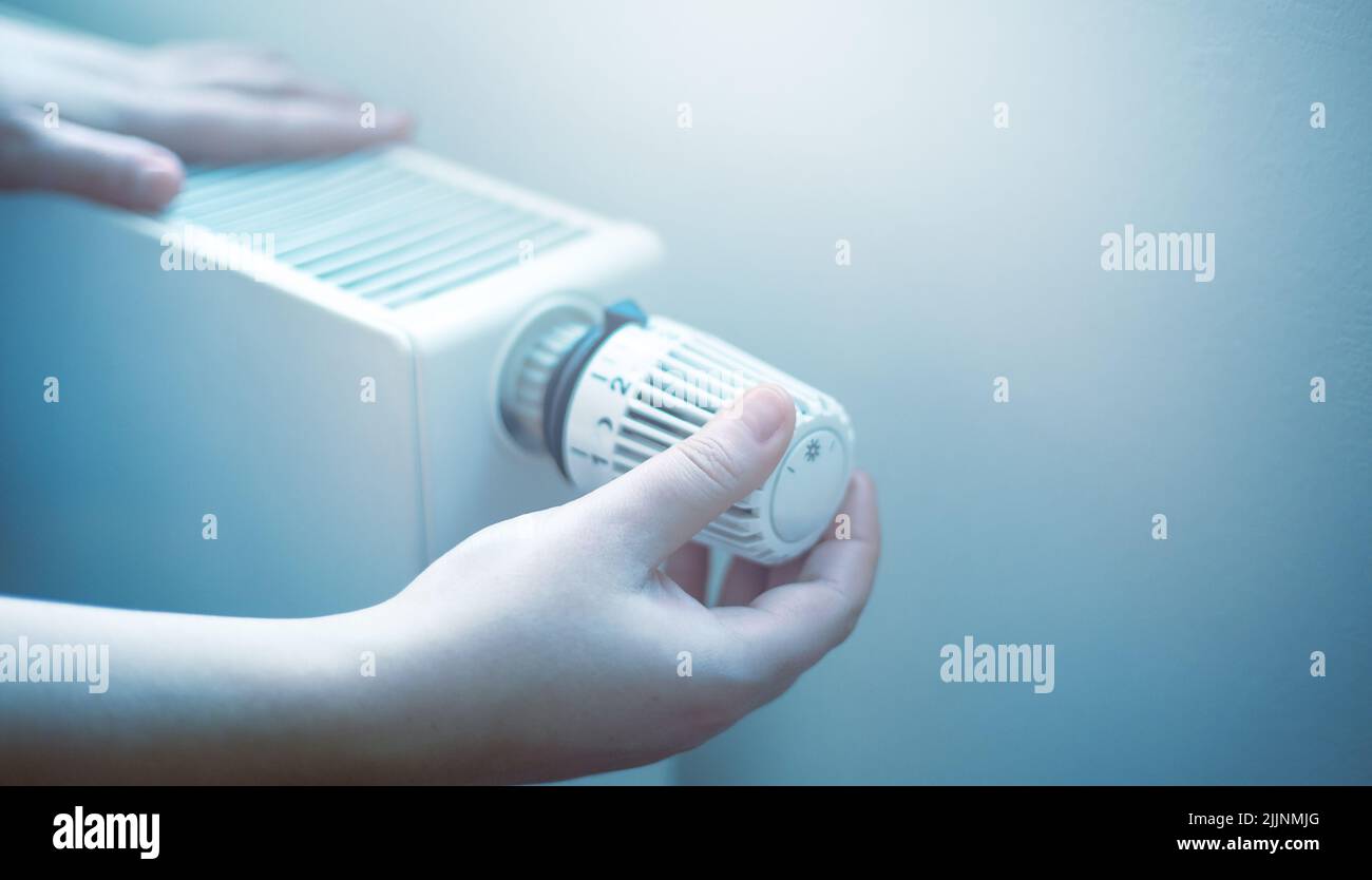 La mano donna regola la temperatura sul radiatore, i prezzi elevati dell'elettricità e del gas, la crisi economica Foto Stock