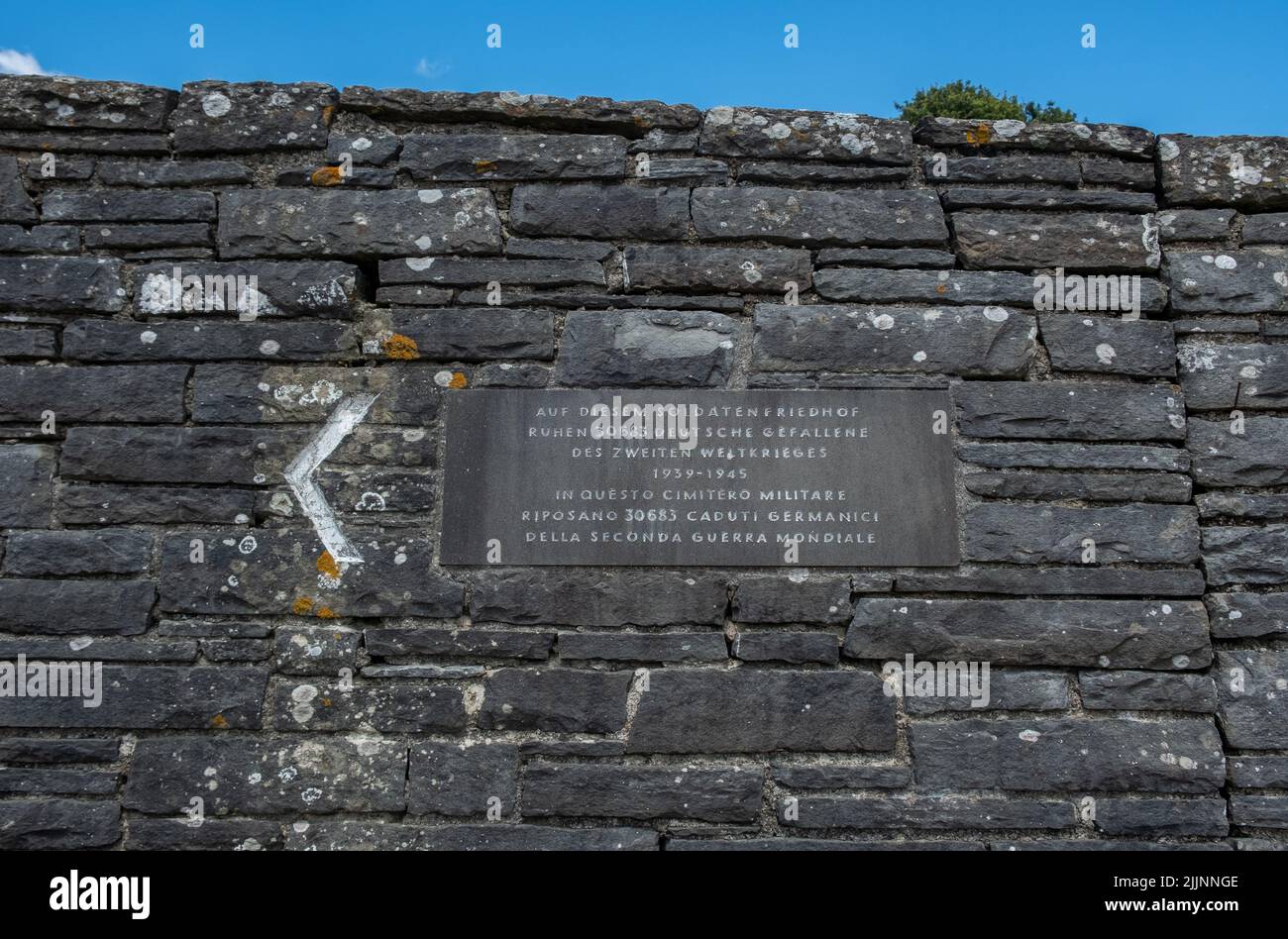 Un cartello sul monumento del cimitero militare tedesco della Futa in Italia sotto il cielo nuvoloso blu Foto Stock