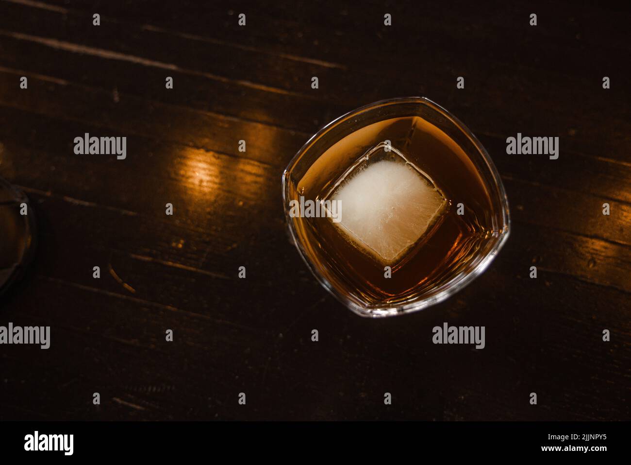 Una vista dall'alto di un bicchiere di whiskey con un cubetto di ghiaccio su un tavolo di legno Foto Stock