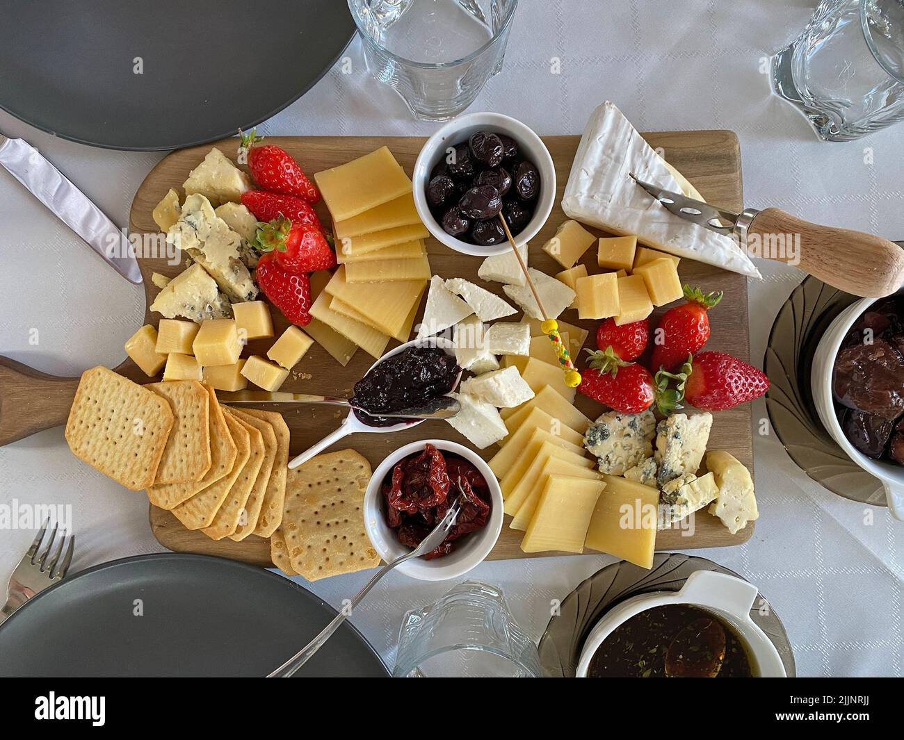 Piatto di formaggi con camembert, brie, dor blue, fragole, pomodori secchi, olive su un tavolo di legno, vista dall'alto. Foto Stock