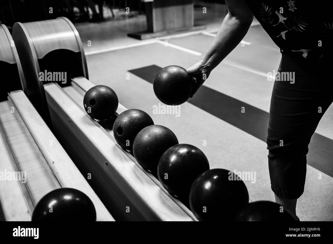 Un primo piano in scala di grigi di un uomo che tiene una palla da bowling per lanciare e giocare Foto Stock