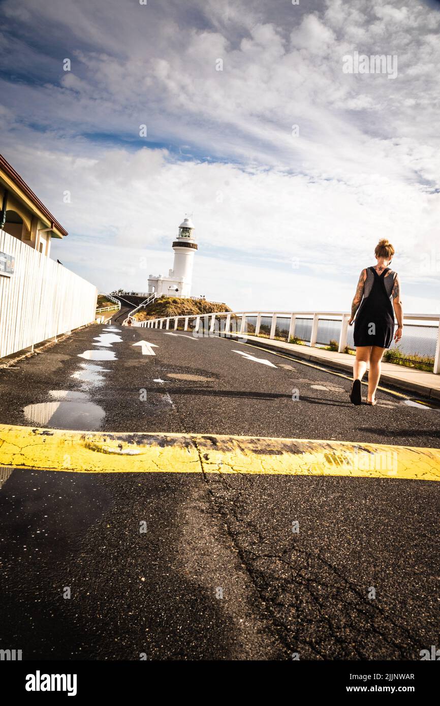 Una vista posteriore del camminare umano sulla strada di fronte al faro in giorno di sole Foto Stock