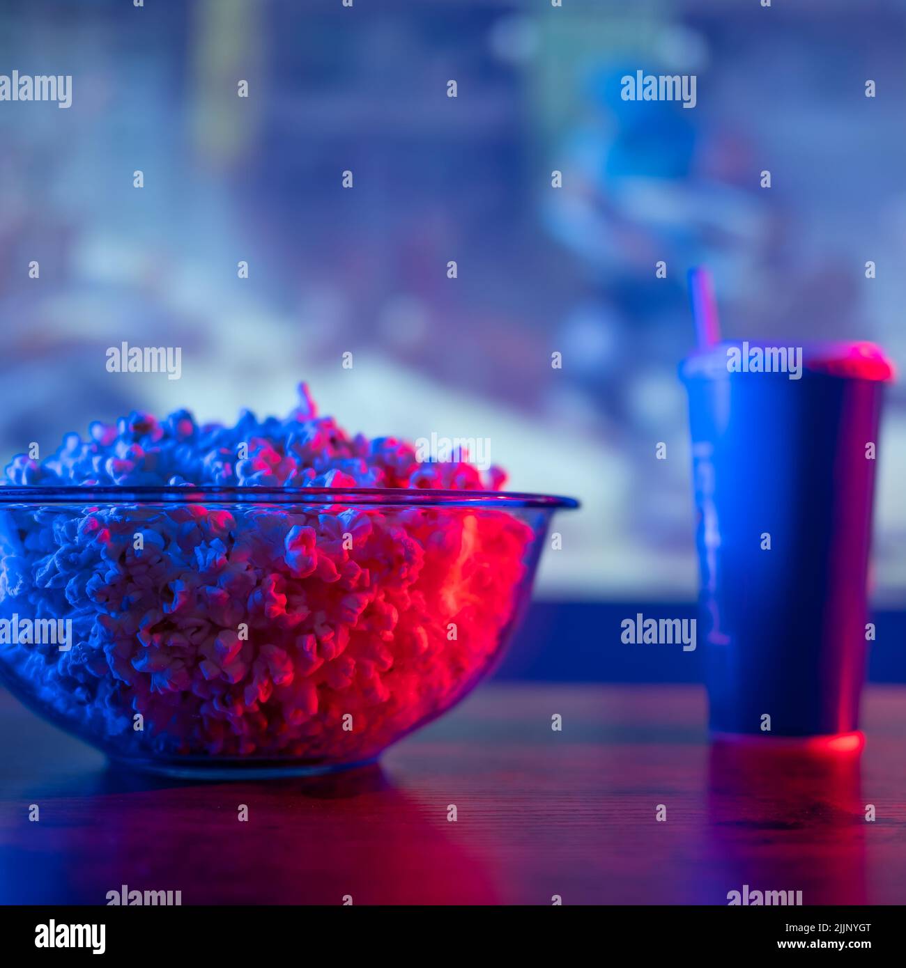 Un set classico per un soggiorno confortevole di fronte alla TV - popcorn, un drink su un tavolo di legno sullo sfondo di un grande schermo TV. Guarda i tuoi preferiti Foto Stock