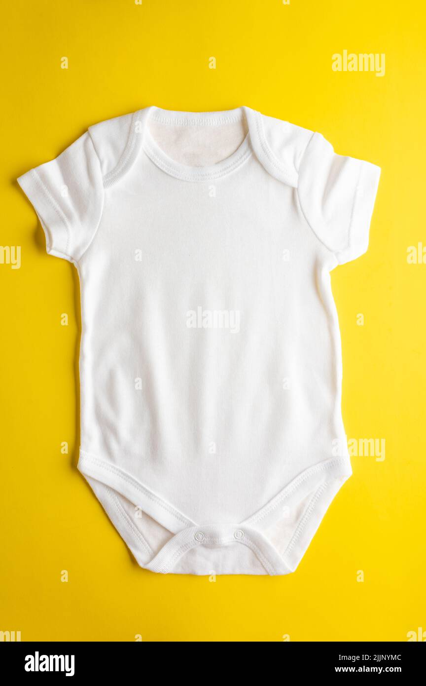 Primo piano. Confortevole tuta bianca in cotone per neonati e bambine su sfondo giallo brillante. Layout piatto per la progettazione e il posizionamento di Foto Stock