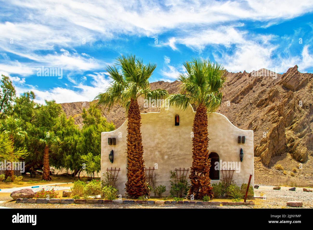 Oasis nel deserto - edificio in Adobe con giardini e palme nella Valle della morte USA con le colline di badlandsd sullo sfondo e il cielo drammatico Foto Stock