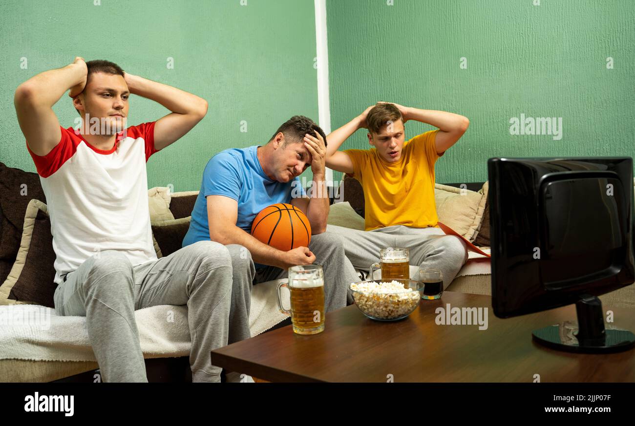 Tre appassionati di basket maschi che guardano il gioco esprimendo delusione Foto Stock