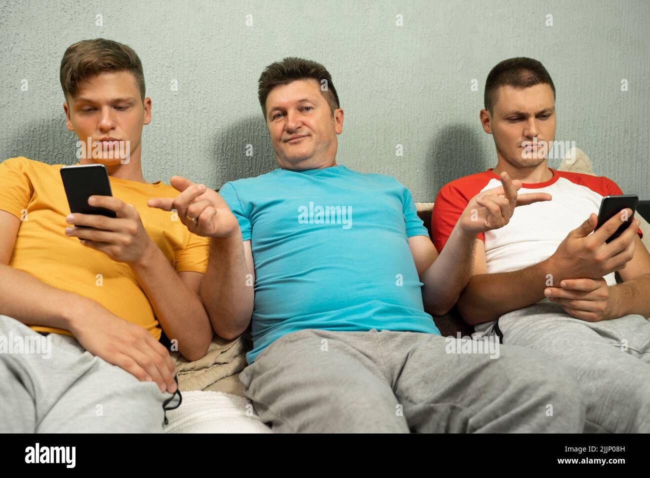 Un maschio che indica la dipendenza del telefono cellulare degli altri due maschi seduti ai lati Foto Stock