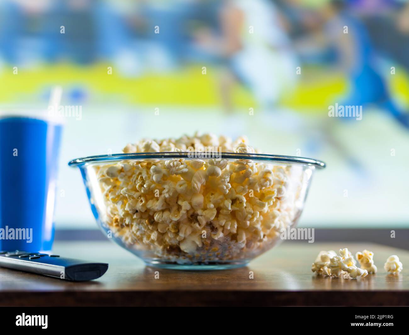 Riposati davanti alla TV, guardando i programmi sportivi. Sullo schermo è presente un gioco di basket. Sul tavolo davanti al televisore c'è una ciotola di popcorn, una soda Foto Stock