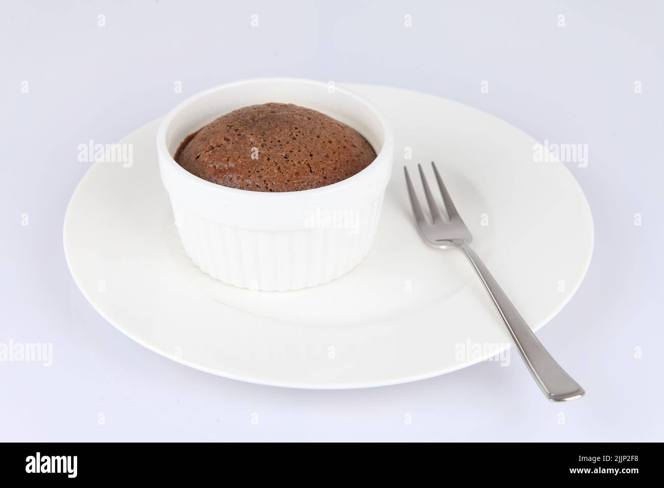 Un souffle di cioccolato in un classico ramekin porcellana bianca su un piatto bianco con forchetta Foto Stock