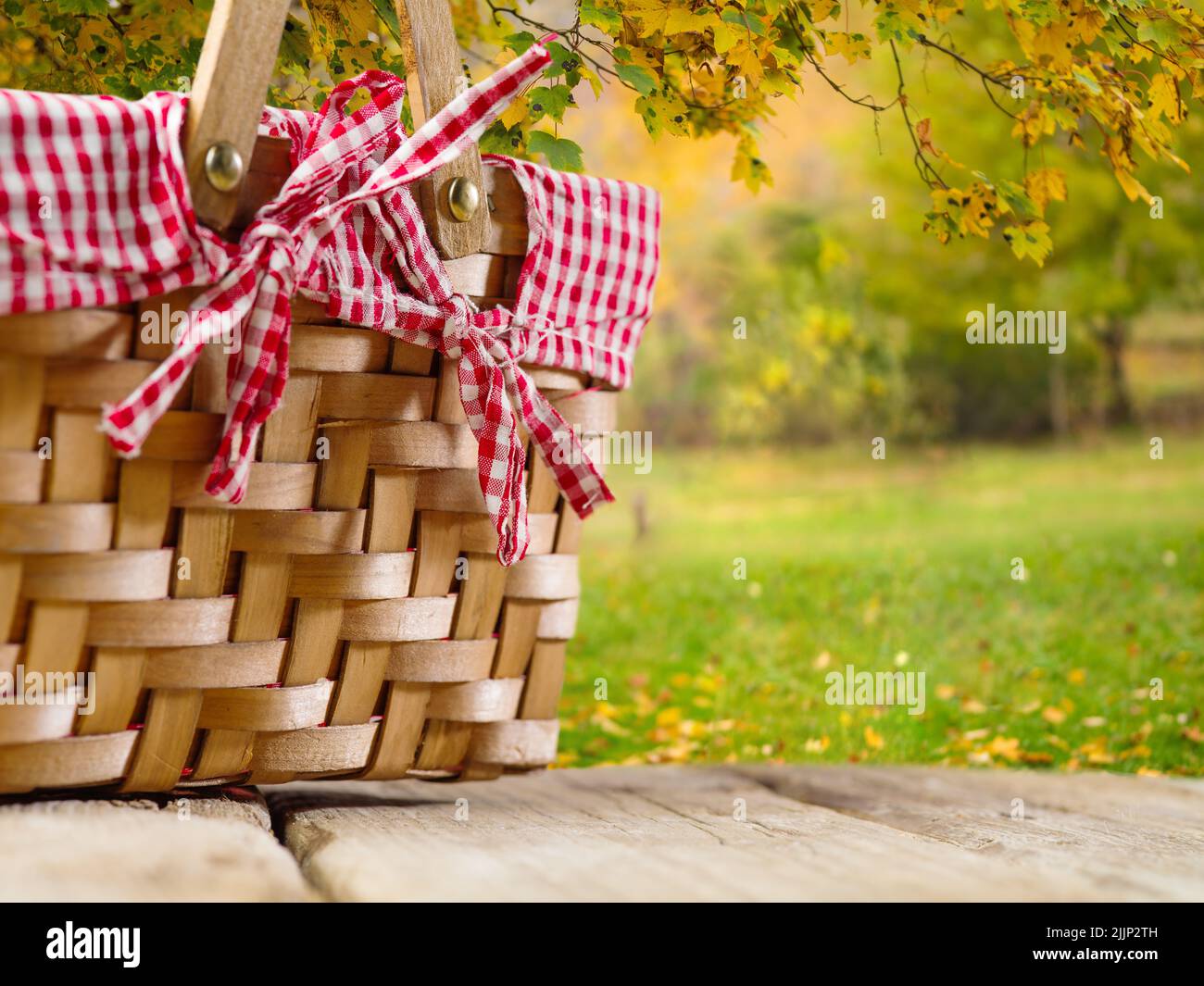 Un accogliente cestino da picnic di paglia su un tavolo di legno sullo sfondo di una pittoresca natura autunnale. Picnic, riposo, tradizioni familiari di giorno di ringraziamento Foto Stock
