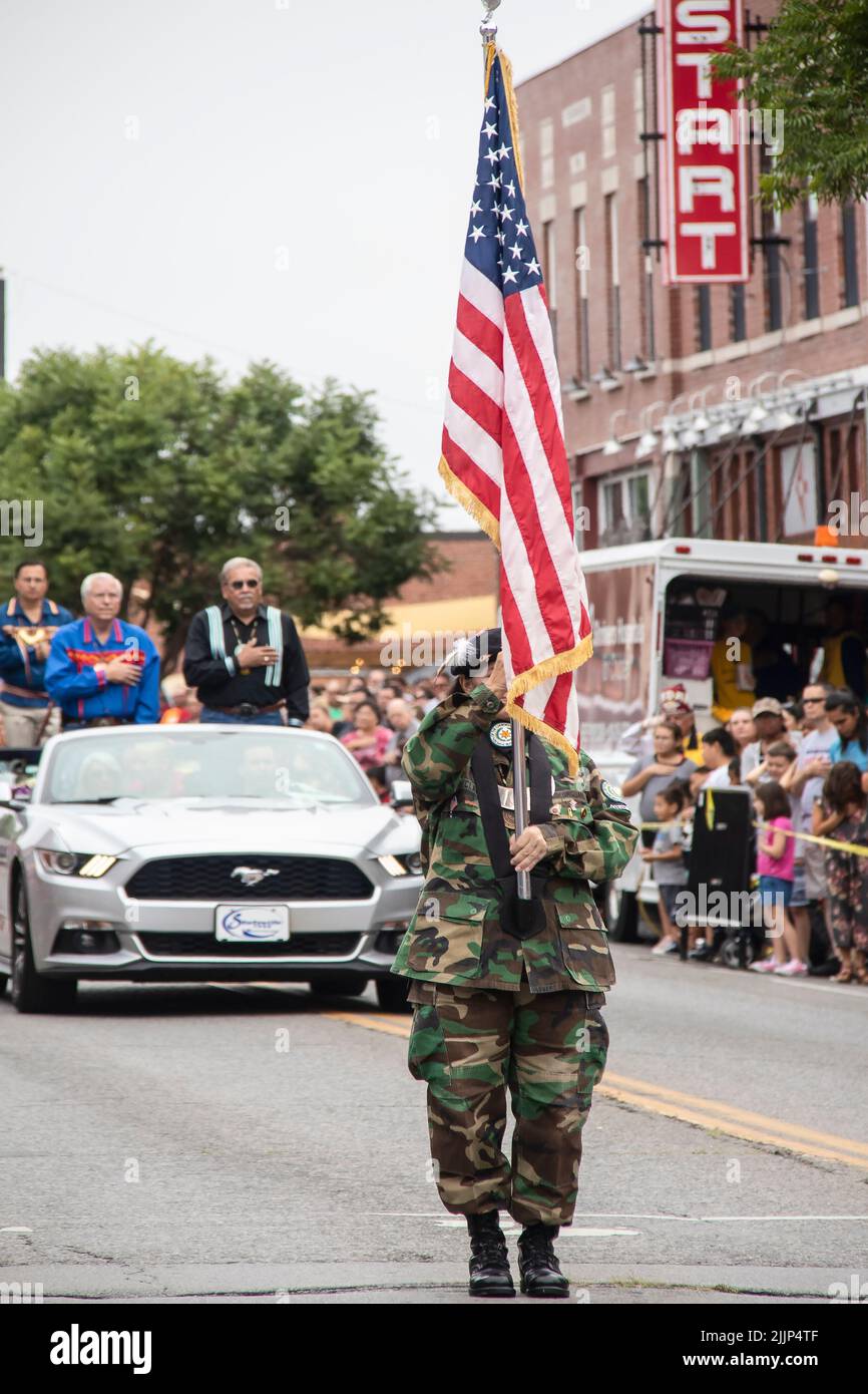 Tahlequah USA 8 31 2019 il membro della Guardia d'onore Cherokee in camos presenta la Bandiera americana in parata mentre gli anziani della tribù in Mustang convertibili e la folla s Foto Stock