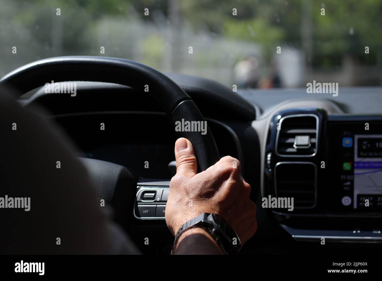 Un primo piano della mano destra di un uomo che poggia sul volante della sua auto con il GPS in funzione Foto Stock