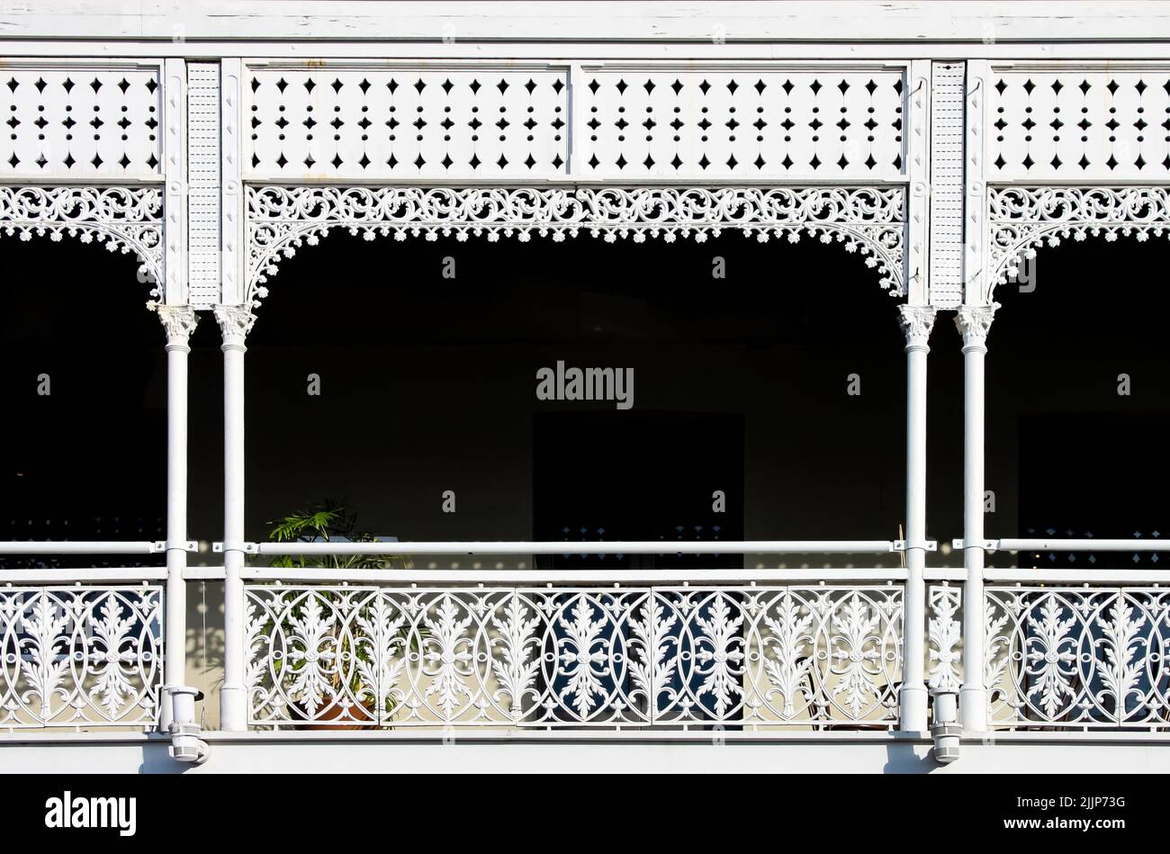 Vittoriano decorativo balcone in ferro battuto con una pianta su di esso, ma per lo più oscurità dietro le ringhiere ornate dipinte di bianco - sfondo Foto Stock