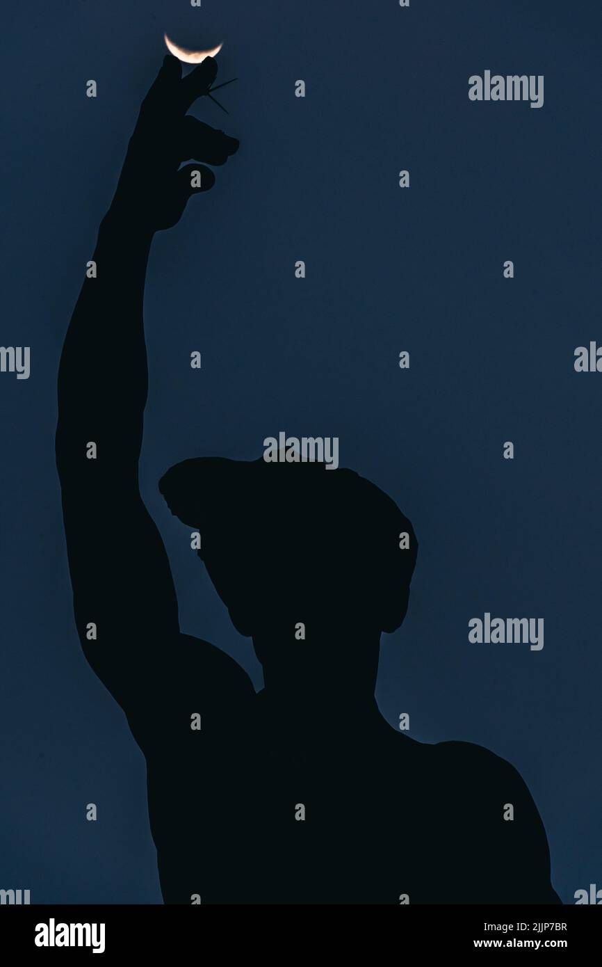 Una silhouette di una statua con una mano che tocca la luna nel cielo Foto Stock Una silhouette di una statua con una mano che tocca la luna nel cielo Foto Stock