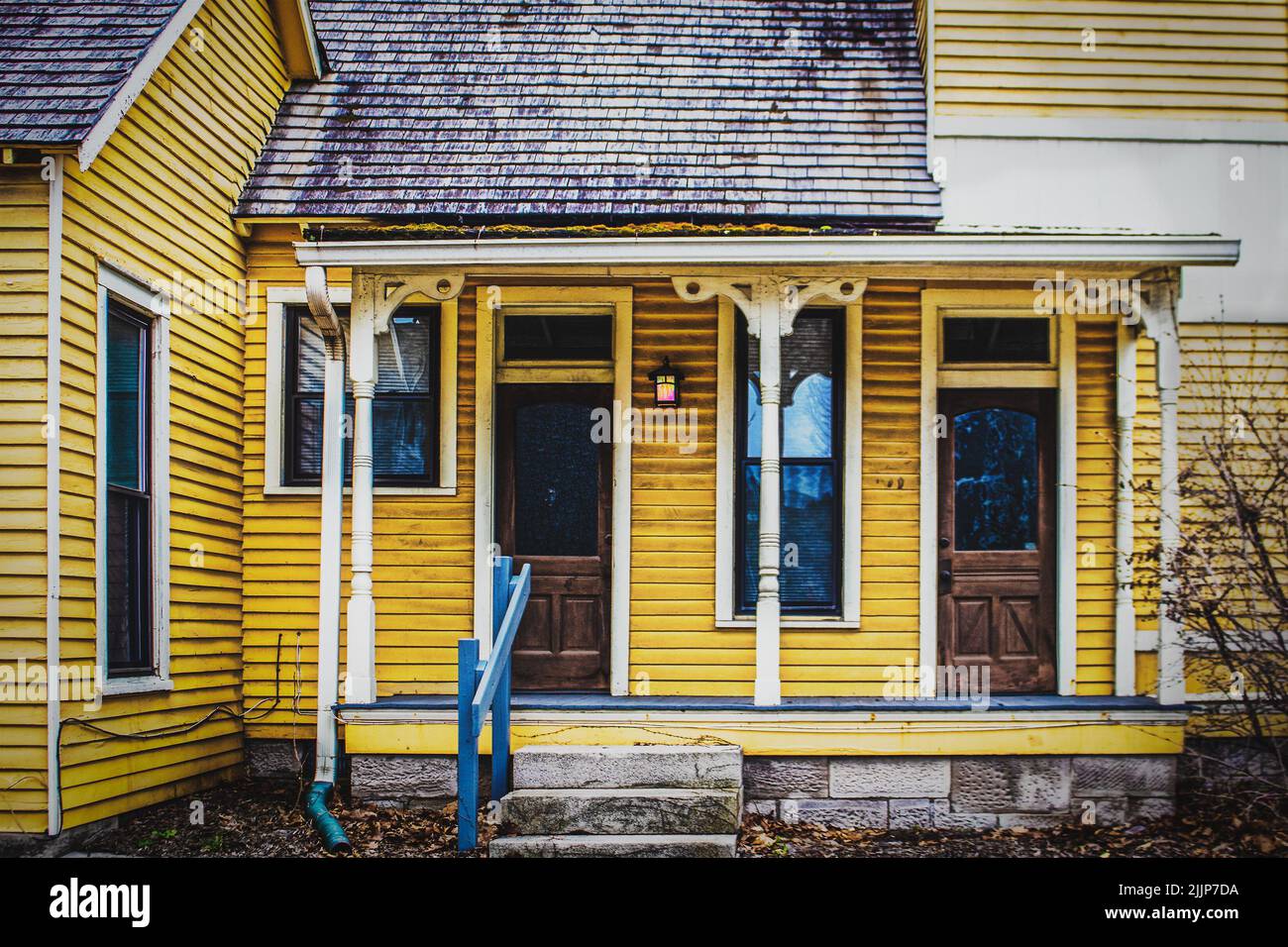 Duplex con telaio giallo vintage con tetto in legno di sassi e portico con vecchie colonne ornate - grungo Foto Stock