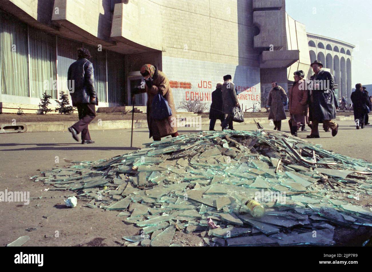 Bucarest, Romania, gennaio 1989. Persone che passano da vetri rotti e detriti in Piazza dell'Università, dall'Intercontinental Hotel, giorni dopo la rivoluzione anti-comunista del dicembre 1989. Sul muro dietro è scritto: 'Giù con il comunismo' & 'buttare via il vostro (partito comunista) ID'. Foto Stock