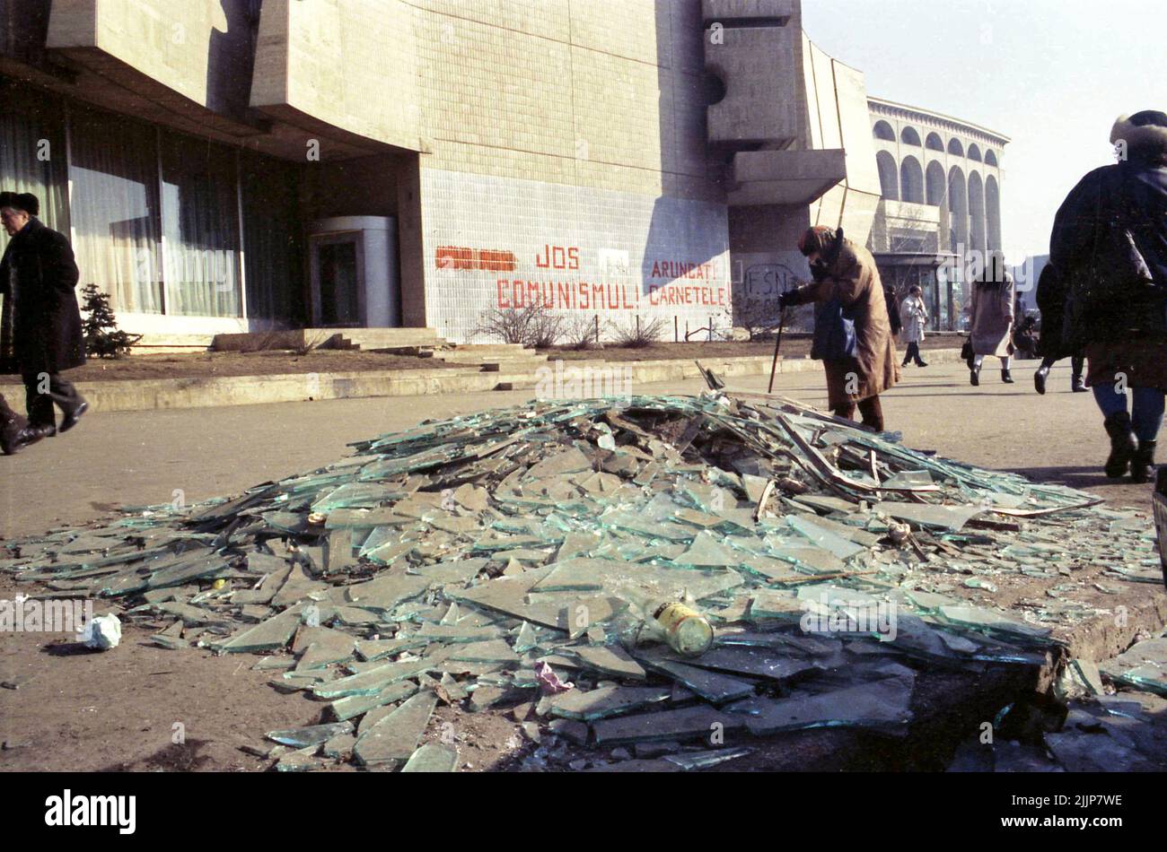 Bucarest, Romania, gennaio 1989. Persone che passano da vetri rotti e detriti in Piazza dell'Università, dall'Intercontinental Hotel, giorni dopo la rivoluzione anti-comunista del dicembre 1989. Sul muro dietro è scritto: 'Giù con il comunismo' & 'buttare via il vostro (partito comunista) ID'. Foto Stock