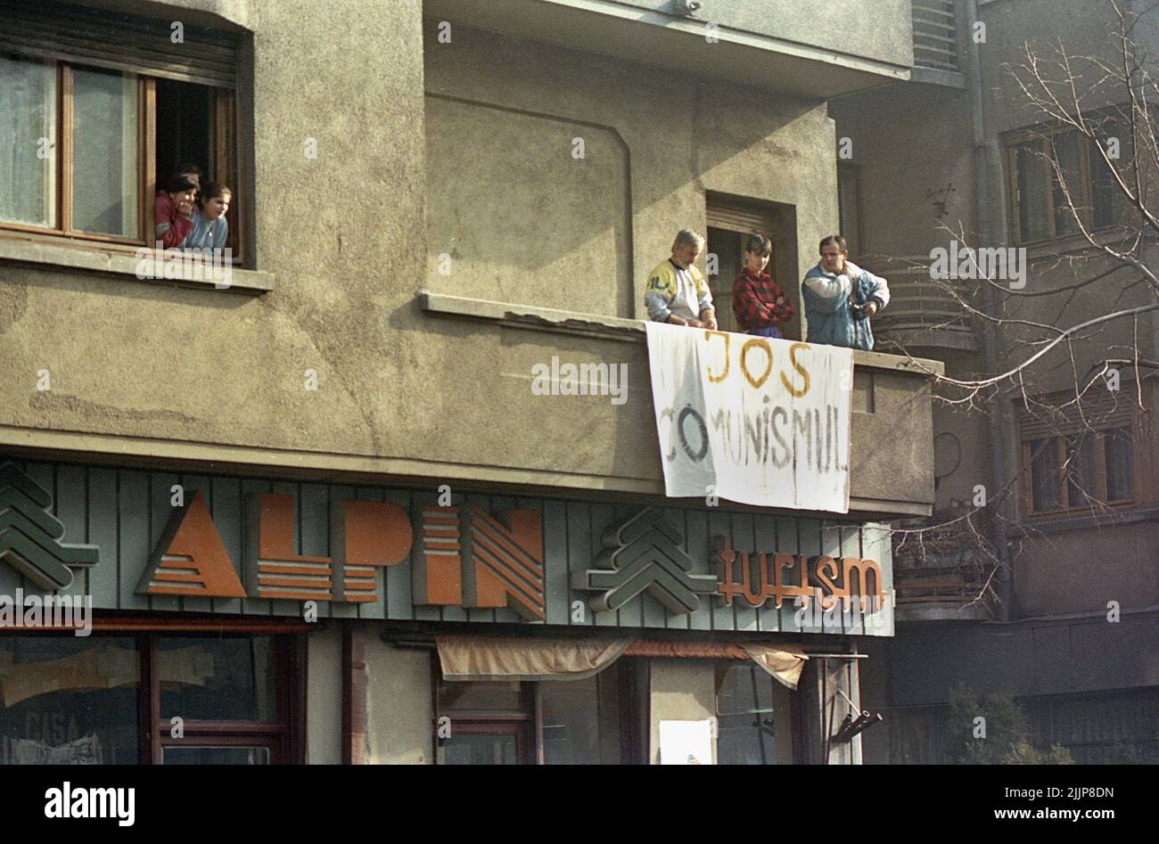 Bucarest, Romania, gennaio 1990. La gente guarda i manifestanti nel centro di Bucarest dal loro appartamento, mostrando una bandiera che dice 'Down with Communism'. Dopo la rivoluzione anti-comunista del dicembre 1989, i disordini civili continuarono, poiché la maggior parte delle nuove persone al potere erano gli ex ufficiali comunisti. Foto Stock