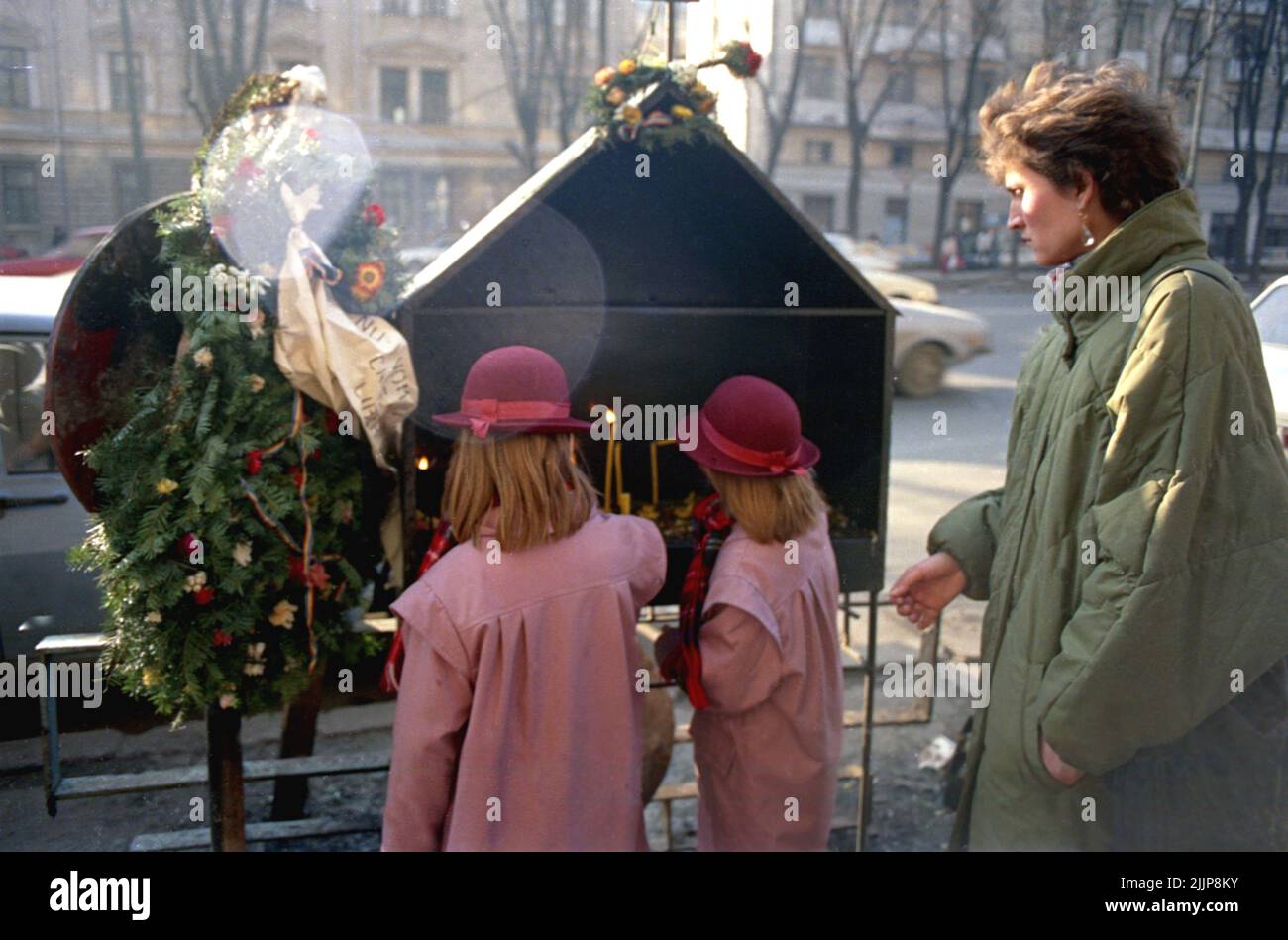 Bucarest, Romania, gennaio 1990. Una madre e le sue figlie illuminarono candele nel piccolo memoriale di fronte a Sala Dalles per le prime vittime della rivoluzione romena anticomunista del dicembre 1989. La morte delle prime sette vittime della rivolta è stata causata da un camion militare che ha colpito i manifestanti. Foto Stock