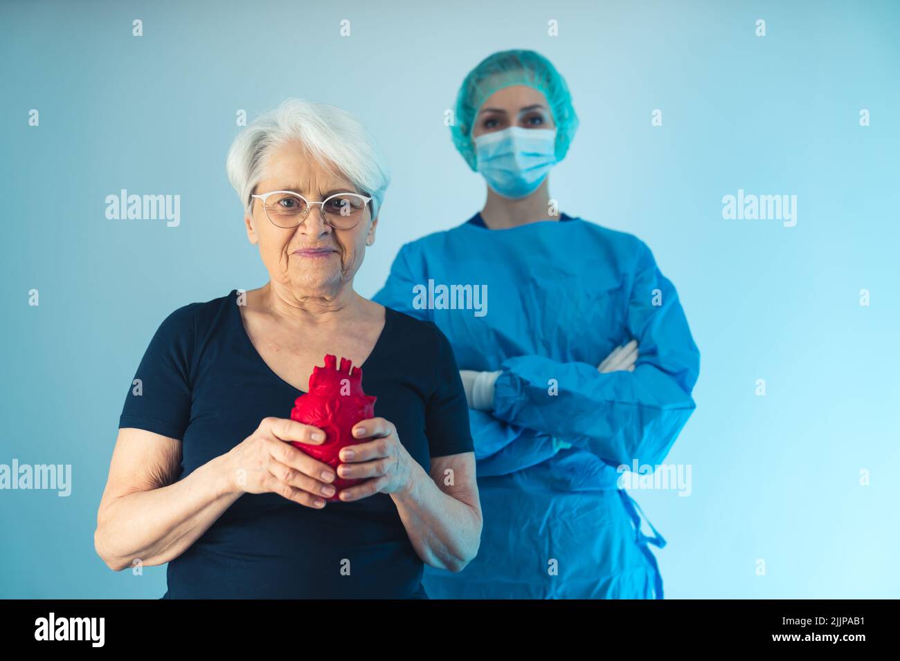 Vecchia donna caucasica in piedi davanti ad un medico chirurgo mentre tiene un cuore artificiale rosso davanti al suo petto. Foto di alta qualità Foto Stock