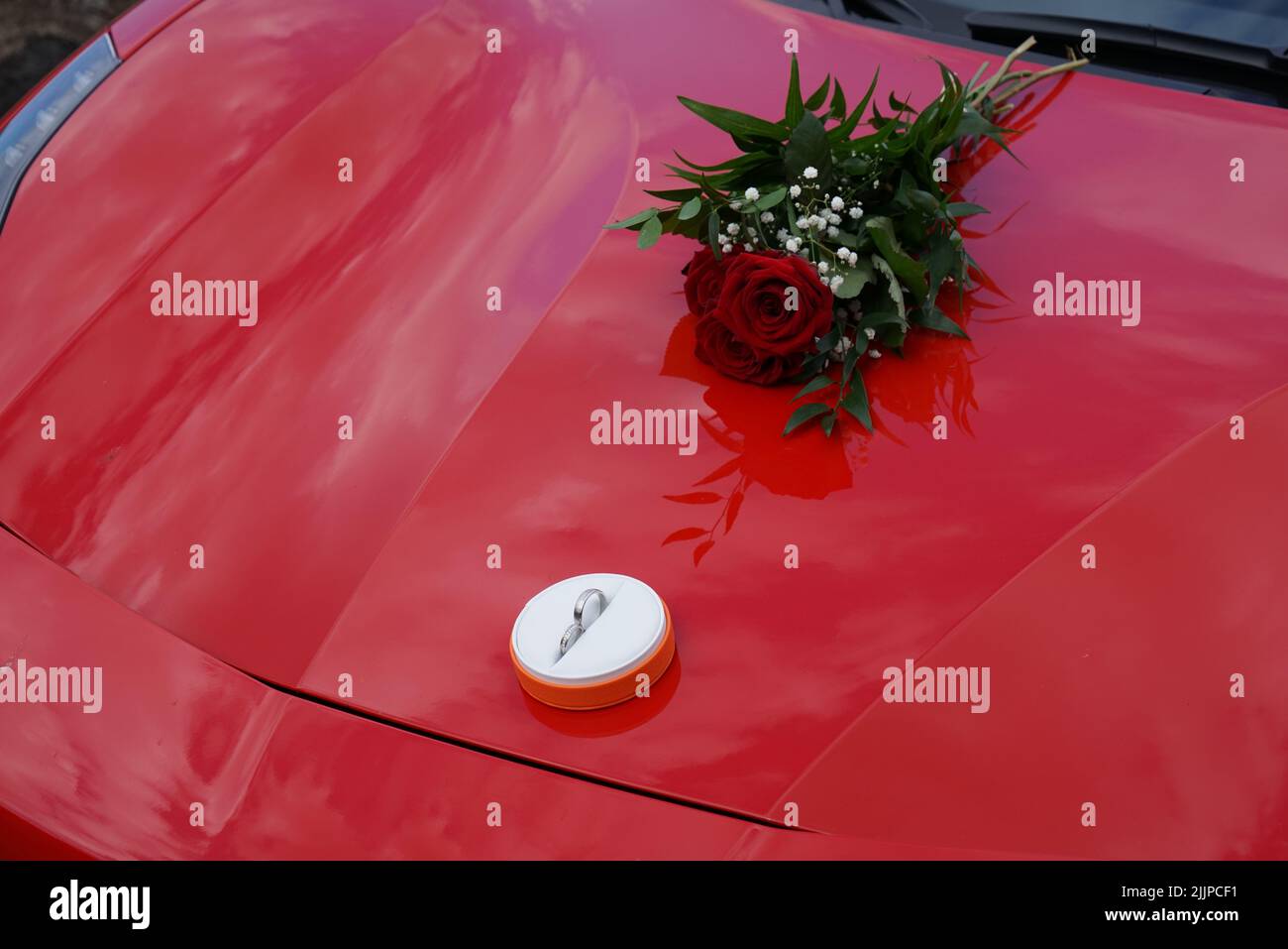 Un set di anelli di aggancio e un bouquet di rose rosse su una Ferrari rossa Foto Stock