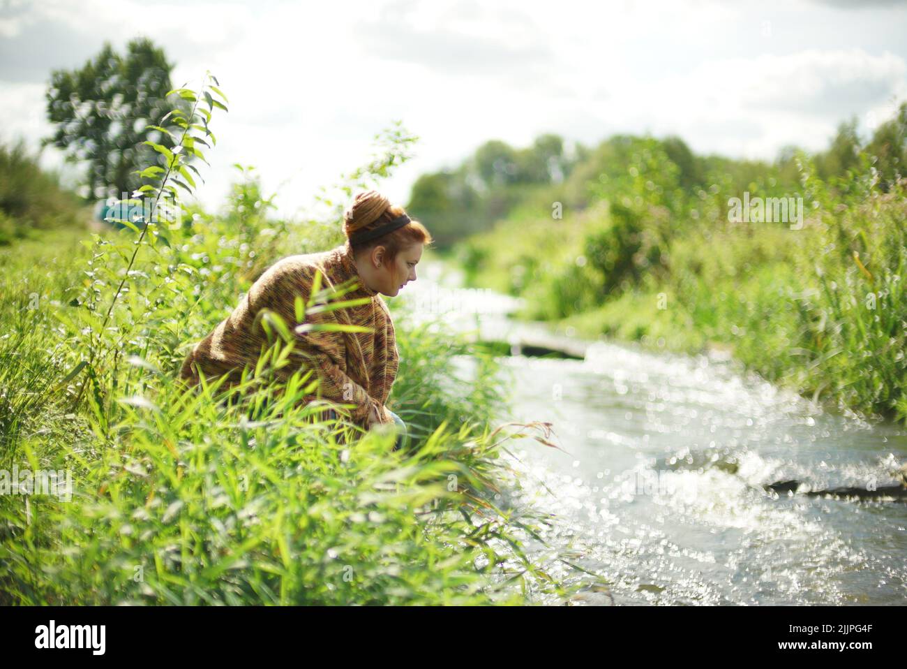 Una femmina bianca con pelo di zenzero in un panino che guarda un fiume dalla riva Foto Stock