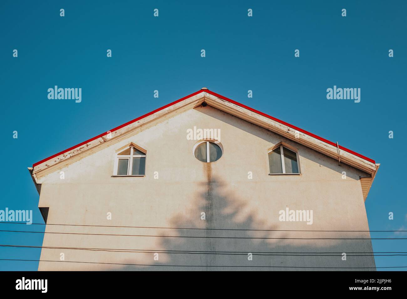Un'immagine ad angolo basso di un edificio con un'ombra di albero sulla sua facciata bianca isolata su uno sfondo blu cielo Foto Stock